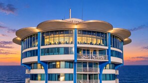 A multi-story building with balconies, large windows, and a view of the sea.