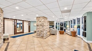 A hotel lobby with a reception desk, a seating area with a sofa and armchairs, a stone pillar, and a tiled floor. - 2BR/2BA • Beachfront • Hot Tub • Pool • Ball Courts • Gym • Fire Pit • 8NE (Daytona Beach)