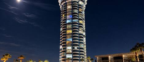 Un hotel alto y cilíndrico con múltiples balcones y una fachada iluminada.