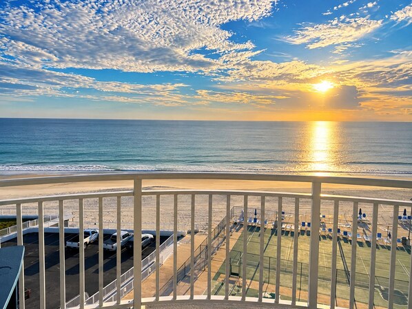 A beach view with a sunset, a parking area, and a fenced sports field.