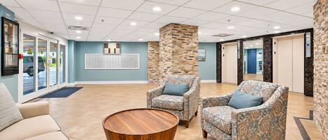 A lobby with two patterned armchairs, a wooden coffee table, and a reception desk.