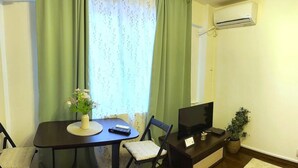 Une petite pièce meublée, comprenant une table à manger, des chaises, un téléviseur et une plante en pot.