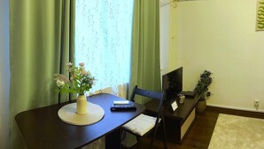 Une petite pièce bien éclairée, avec une table à manger, des chaises, un téléviseur et une plante en pot.