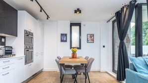 A modern kitchen with white cabinets, a built-in oven, and a dining area with a wooden table and chairs. - Bright 2BR - 2Bath Apt with Balcony | Kentish Town (Greater London)