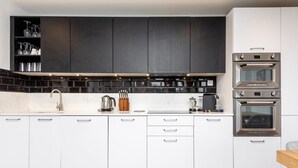 A modern kitchen with white cabinets, black backsplash, and stainless steel appliances. - Bright 2BR - 2Bath Apt with Balcony | Kentish Town (Greater London)