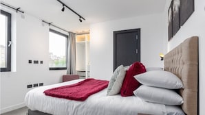A modern bedroom with a bed, bedside table, and a view of the city through the window. - Bright 2BR - 2Bath Apt with Balcony | Kentish Town (Greater London)