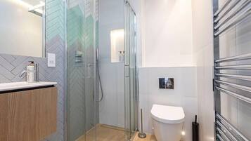 A modern bathroom with a glass shower enclosure, a white toilet, and a wooden vanity.