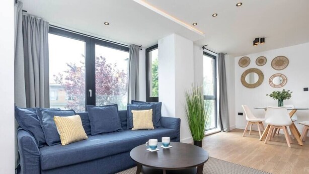 Una sala de estar moderna con un sofá azul, una mesa de centro redonda y un comedor con mesa y sillas blancas.