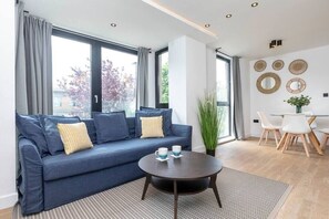 Un salon moderne avec un canapé bleu, une table basse ronde et un coin repas comprenant une table et des chaises blanches.