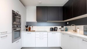 Una cocina moderna con armarios blancos, horno empotrado y cafetera.