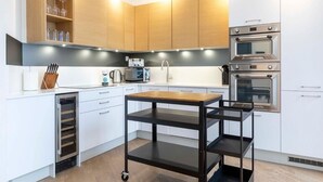 A modern kitchen with white cabinets, a built-in oven, a microwave, and a wine rack.