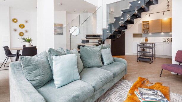 A modern living room with a light blue sofa, a dining area, and a kitchen.