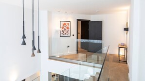 A modern interior with a glass railing, a framed artwork, and a dark door.