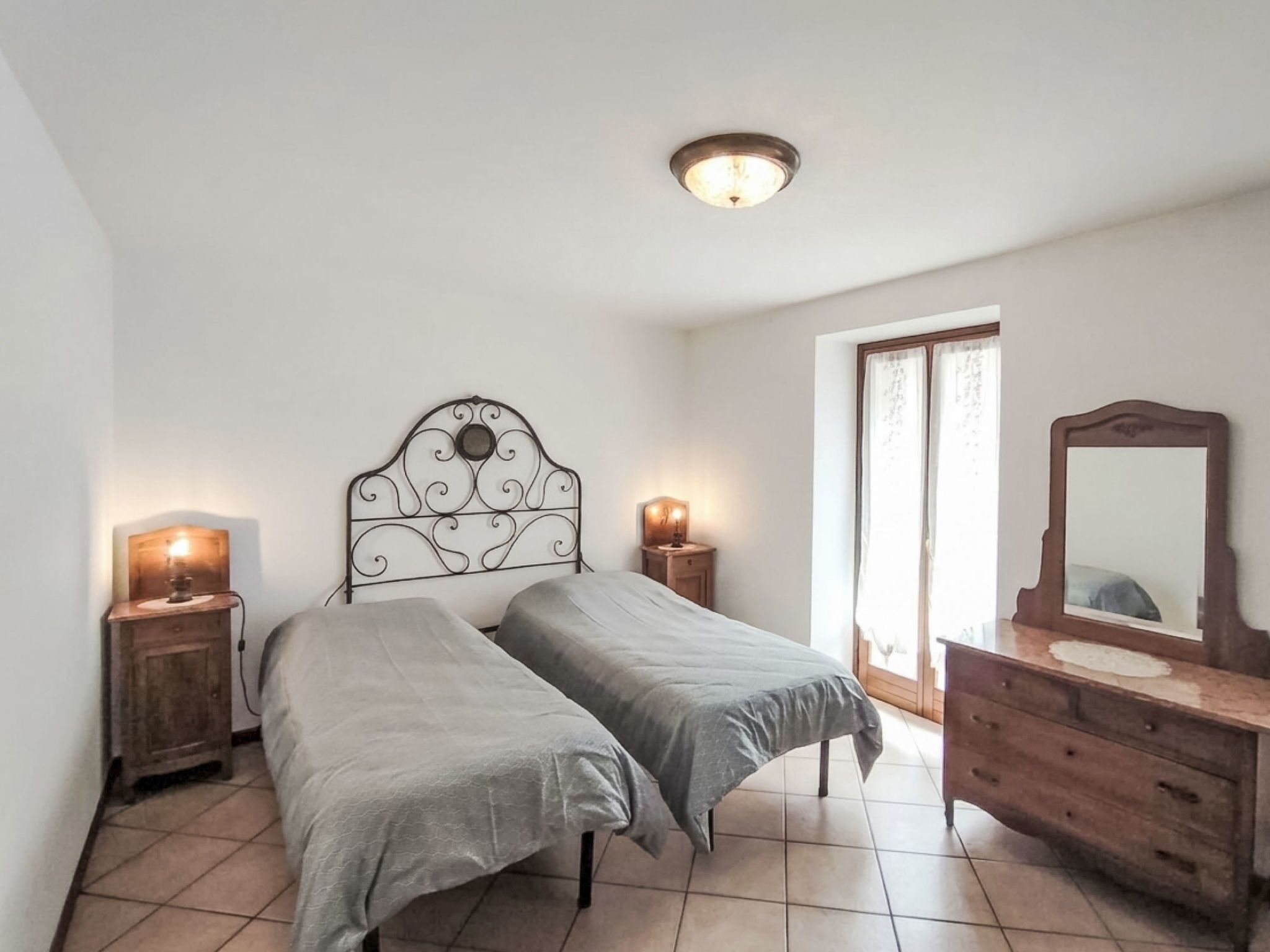 A bedroom with two beds, a dresser, a mirror, and a ceiling light.