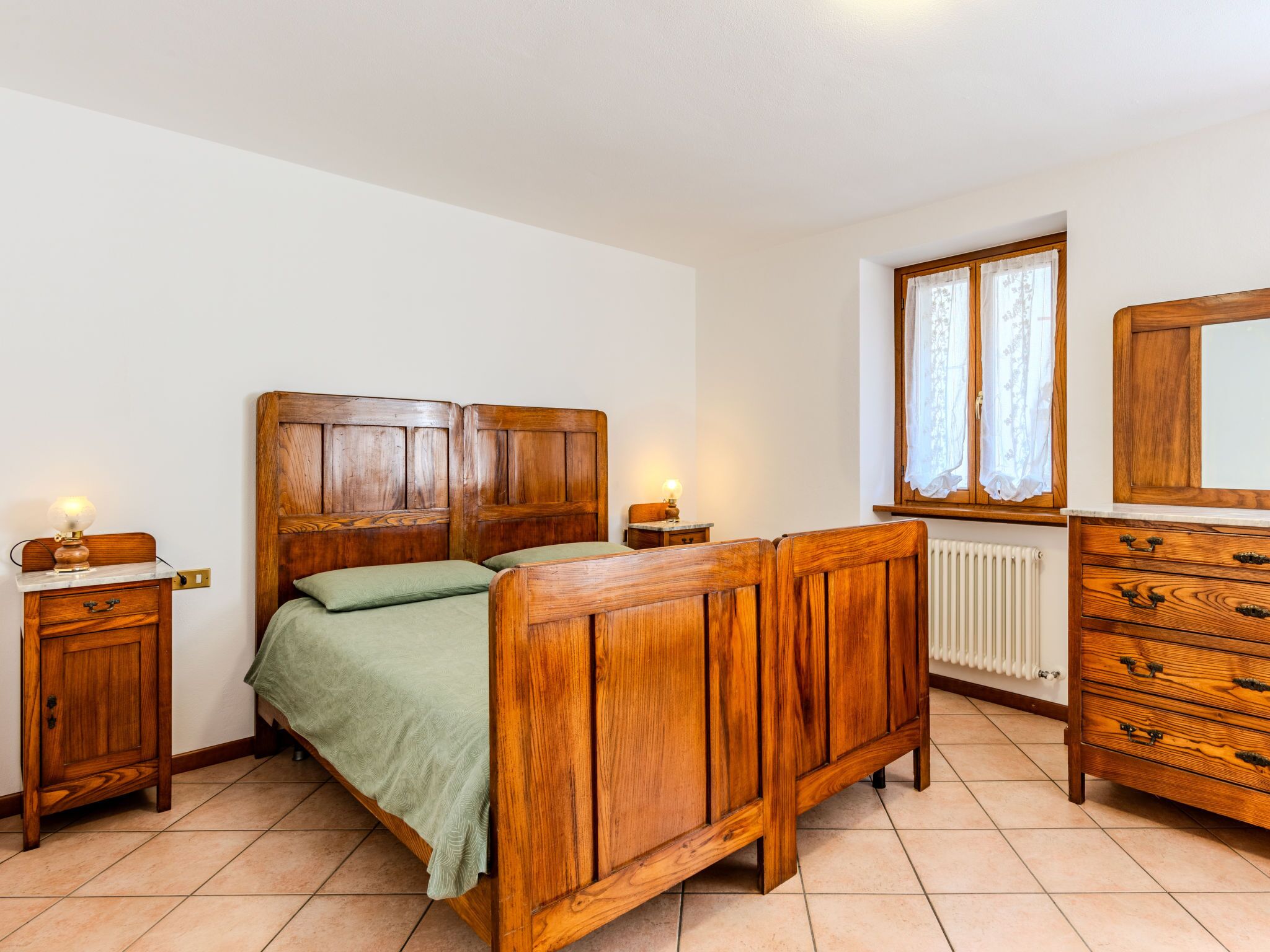 Un dormitorio con una cama de madera, un aparador, una mesita de noche y una ventana con cortinas.