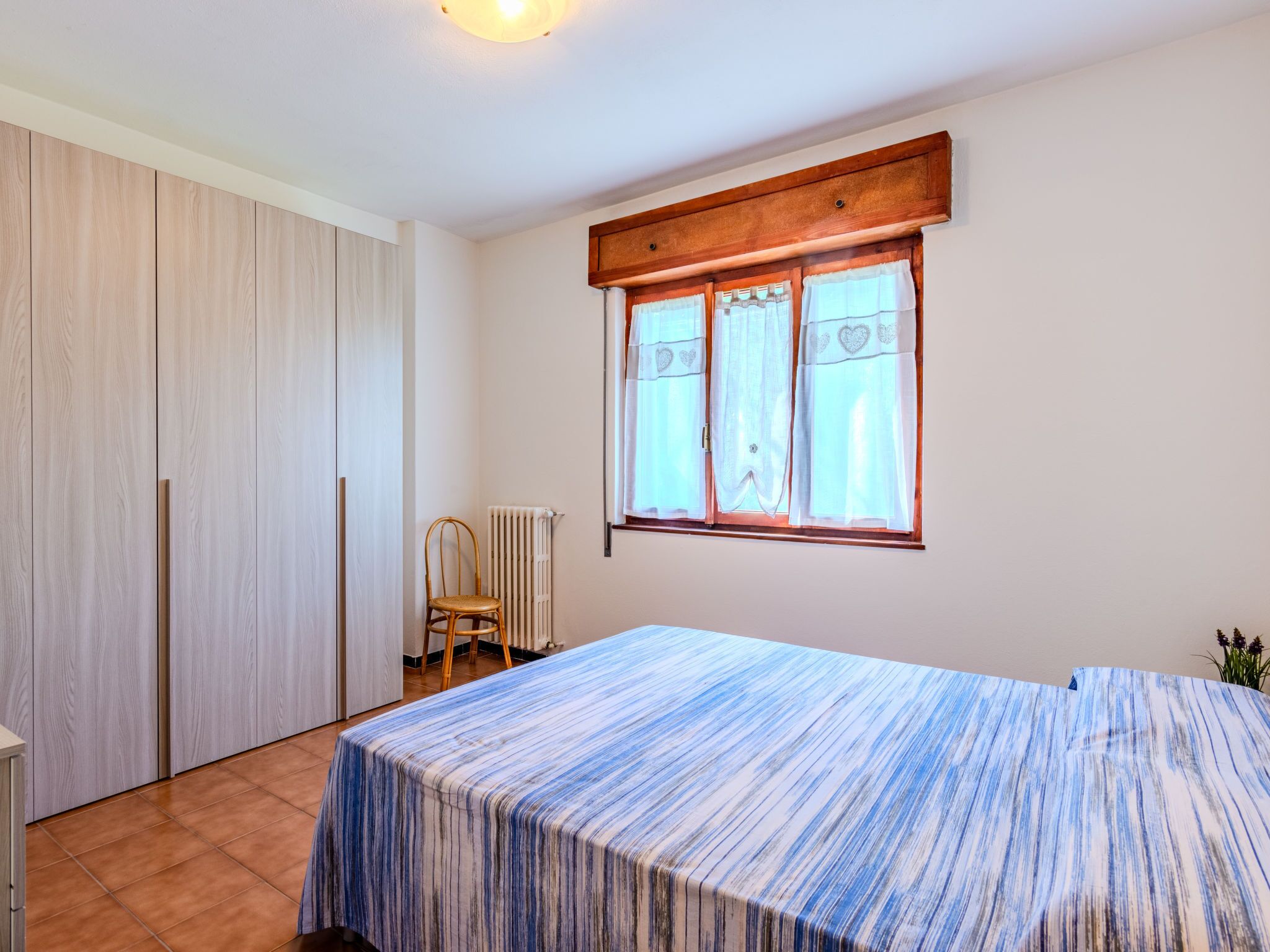 Une pièce comprenant un lit, une chaise, un radiateur et une fenêtre avec des rideaux.