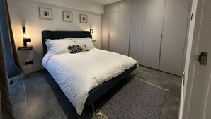 Et moderne soveværelse med en stor seng, indbygget skab og sengeborde med lamper.