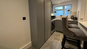 Et moderne køkken med lysegrå skabe, indbygget ovn og en bar med barstole.