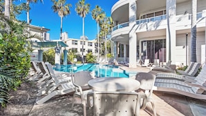 A poolside area with lounge chairs and a table, surrounded by palm trees and a building with balconies. - Surfers Paradise Studio with Ocean Views (Surfers Paradise)