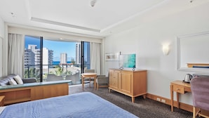 A hotel room with a large bed, a desk, a chair, a wardrobe, and a view of the cityscape through large windows. - Surfers Paradise Studio with Ocean Views (Surfers Paradise)