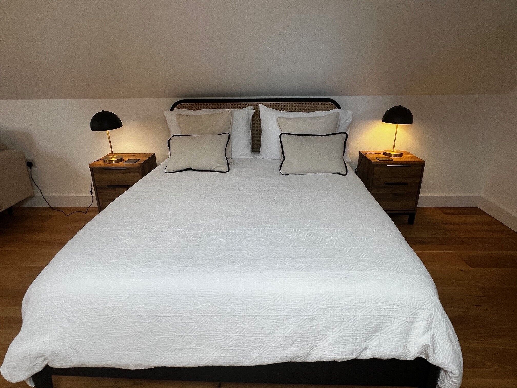 Een opgemaakt bed met een witte deken, twee nachtkastjes met lampen, en een hoofdbord.