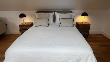 Een opgemaakt bed met een witte deken, twee nachtkastjes met lampen, en een hoofdbord.