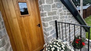 A wooden door with a small window, a stone wall, and a metal railing with flowers. - Studio-King Bed-Wye Valley Views (Bettws Newydd, Usk)