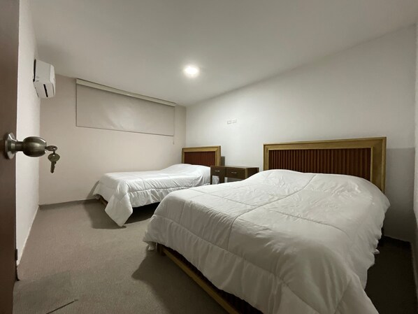 A hotel room with two single beds, a wooden headboard, a small desk, and a wall-mounted air conditioning unit. - GL Hostal (Barranquilla)