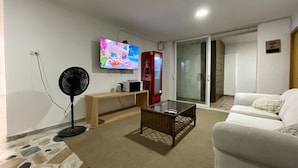 A living room with a flat-screen TV, a fan, a coffee machine, and a sofa. - GL Hostal (Barranquilla)