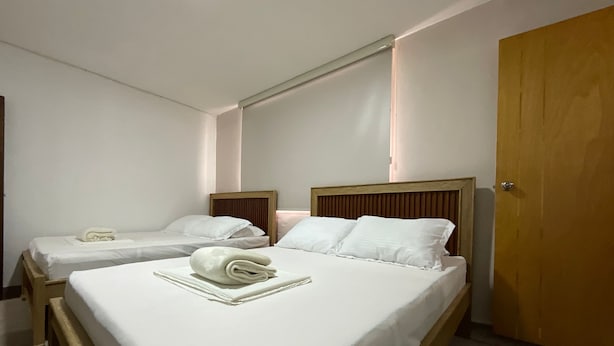 A hotel room with two single beds, a wooden headboard, a wooden door, and a white wall. - GL Hostal (Barranquilla)