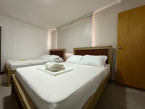 A hotel room with two single beds, a wooden headboard, a wooden door, and a white wall. - GL Hostal (Barranquilla)