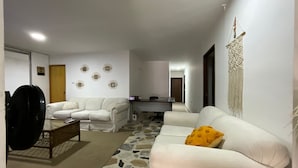 A living room with a white sofa, a coffee table, and a patterned rug. There is a door and a wall with decorative eye motifs. - GL Hostal (Barranquilla)
