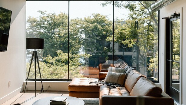 A modern living room with a large window, a sofa, a coffee table, and a floor lamp. - Kroger Lofts | Unit A | Rooftop Pool | Lake Views (Charlevoix)