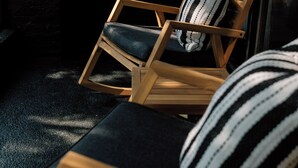 A wooden chair with a black cushion and a striped pillow, positioned near a glass door. - Kroger Lofts | Unit A | Rooftop Pool | Lake Views (Charlevoix)