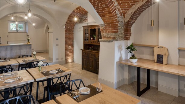A restaurant with brick arches, wooden tables, and hanging light fixtures. - Casa Calleri by Interhome (Briaglia)