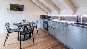A modern kitchen with a dining area, featuring a built-in oven, a kettle, and a flat-screen TV mounted on the wall. - Casa Calleri by Interhome (Briaglia)