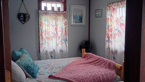 A bedroom with a bed, pillows, a fan, and floral curtains.