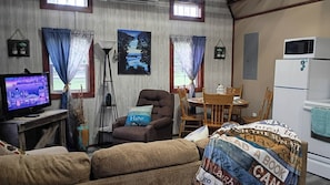A cozy living room with a television, a sofa, a chair, a table, and a refrigerator.