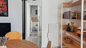Een moderne woonkamer met een houten eettafel, een boekenkast en uitzicht op de aangrenzende badkamer.