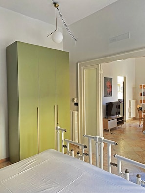 Un dormitorio con una cama, un armario verde, un radiador y un televisor en la habitación contigua.