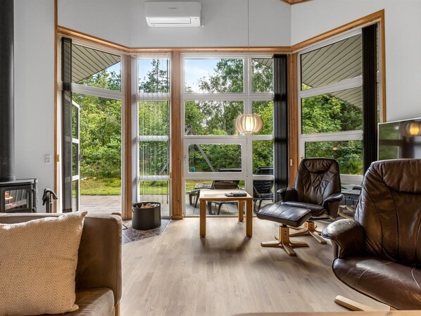 A modern living room with a large glass door leading to a deck, a fireplace, leather sofas, and a hanging light fixture.