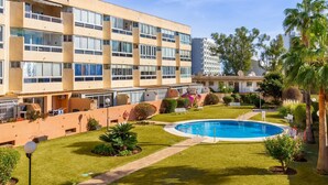 Un edificio de varios pisos con piscina, rodeado de céspedes cuidados y palmeras.