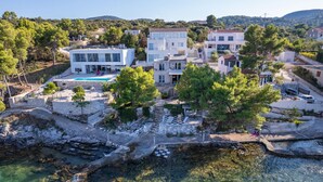 Une propriété située sur la côte, comprenant plusieurs bâtiments, une piscine et un rivage rocheux.