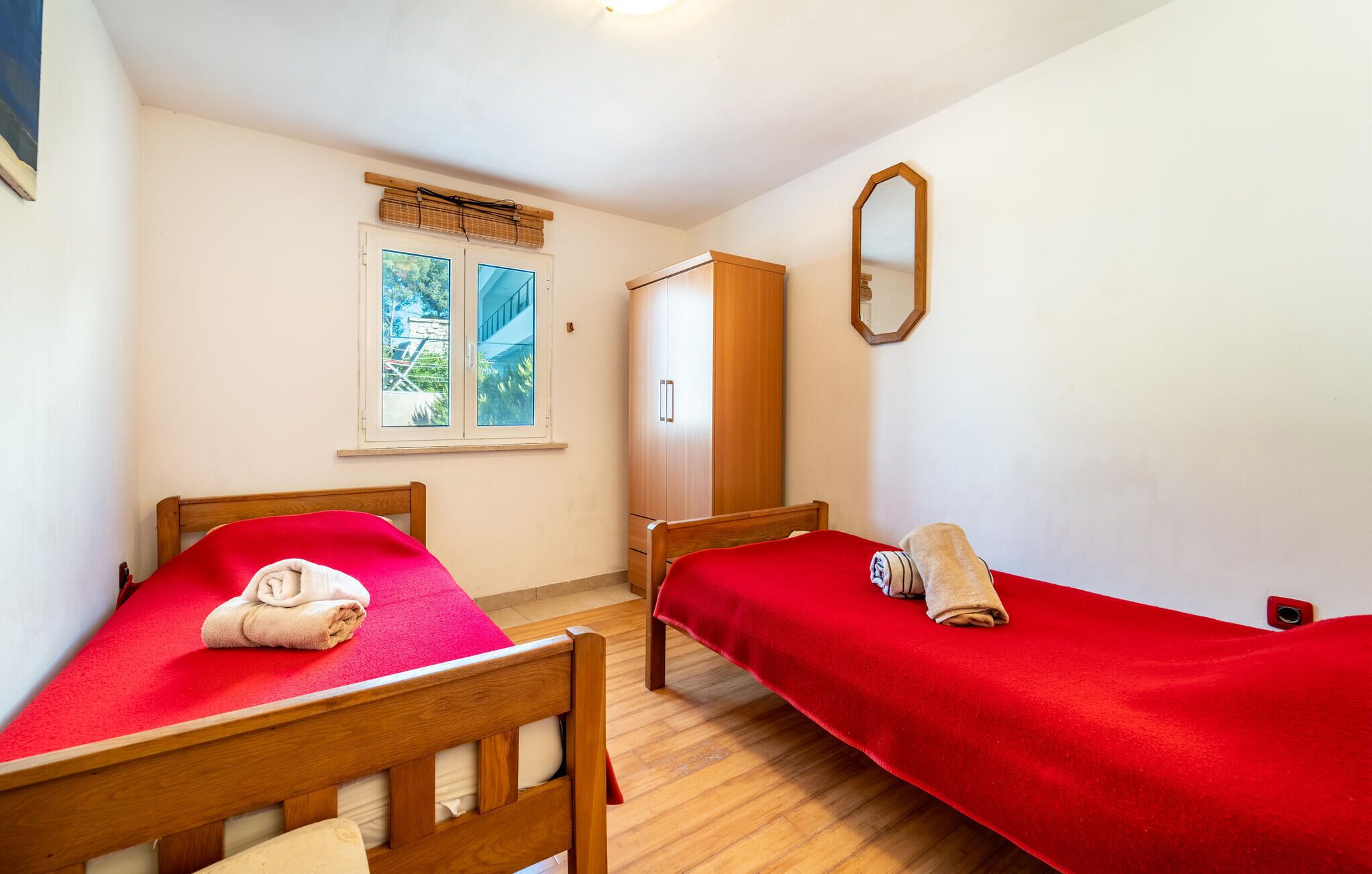 A small, clean room with two single beds, a window with a view, and a mirror on the wall.