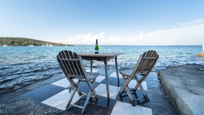 Une table en bois avec deux chaises, placée sur une terrasse carrelée au bord de la mer, et une bouteille de champagne posée sur la table.