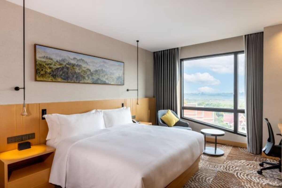 A hotel room with a large bed, a view of the city, and a painting on the wall.