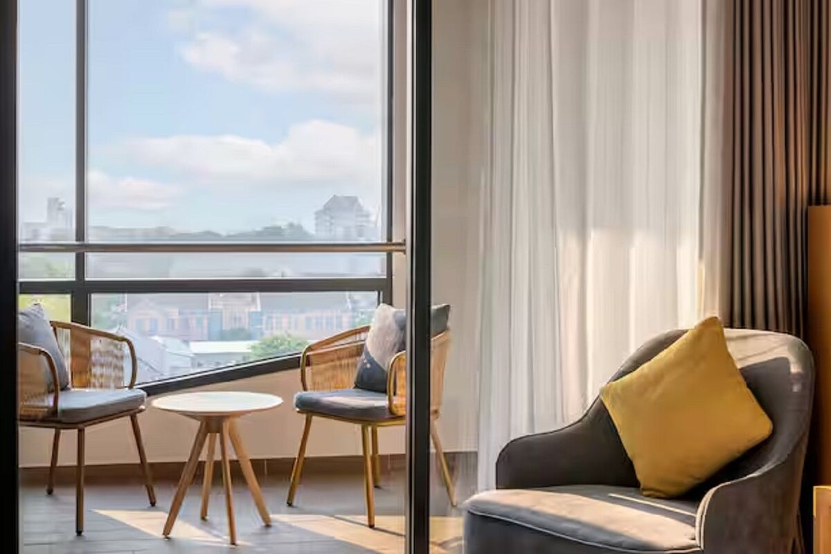 A modern room with a large window, two chairs, a small table, and a sofa with a yellow pillow.