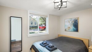 A bedroom with a bed, a window, a painting, and a mirror.