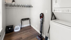 A laundry room with a stacked washer and dryer, a vacuum cleaner, a drying rack, and a fan. - Mid-Century Connection | Nestled Amid Universities (Sioux Falls)