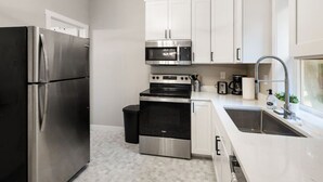 A modern kitchen with stainless steel appliances, white cabinetry, and a large window providing natural light. - Mid-Century Connection | Nestled Amid Universities (Sioux Falls)